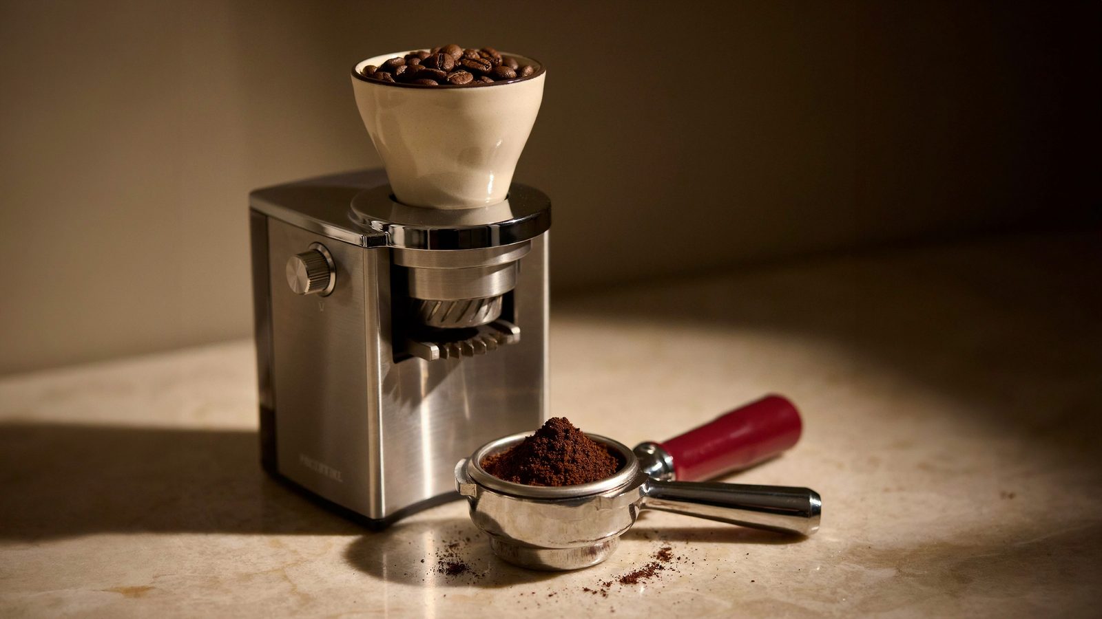 A premium flat-burr espresso grinder with a single-dose cup and fine espresso grounds piled in a portafilter below it, burrs and metal detail visible, moody warm light