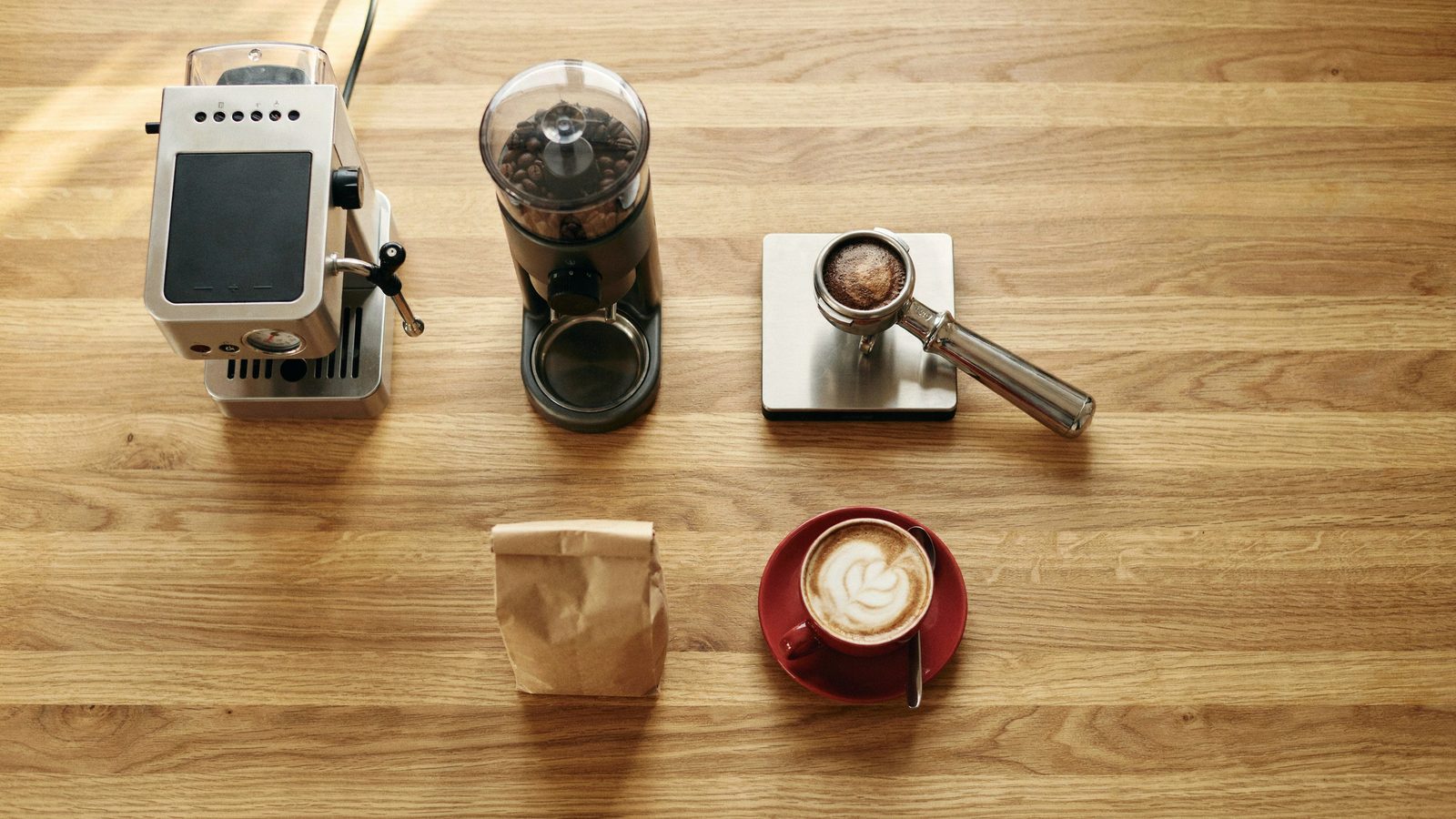 Overhead view of a home espresso setup: espresso machine, grinder, scale with portafilter, bag of beans and a cappuccino in a red cup